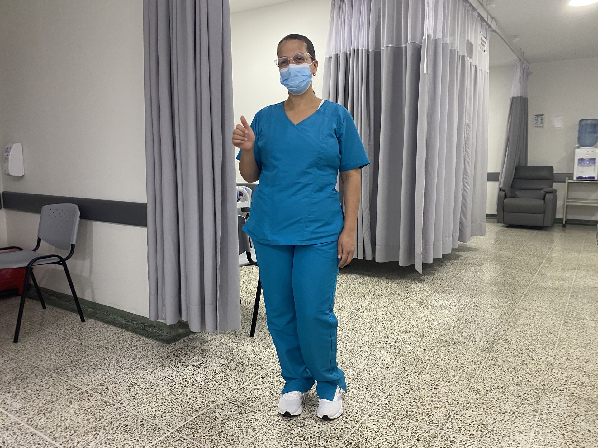 Profesional de la salud con uniforme azul de pie en un área clínica hospitalaria